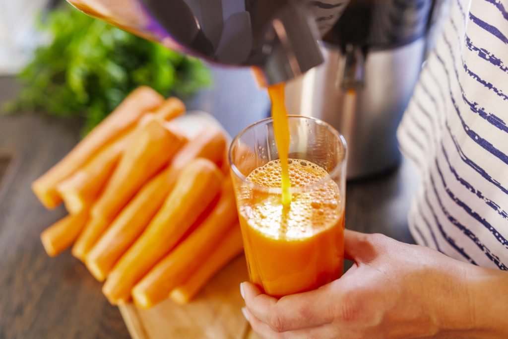 Imagem de mulher enchendo copo com suco de cenoura fresco