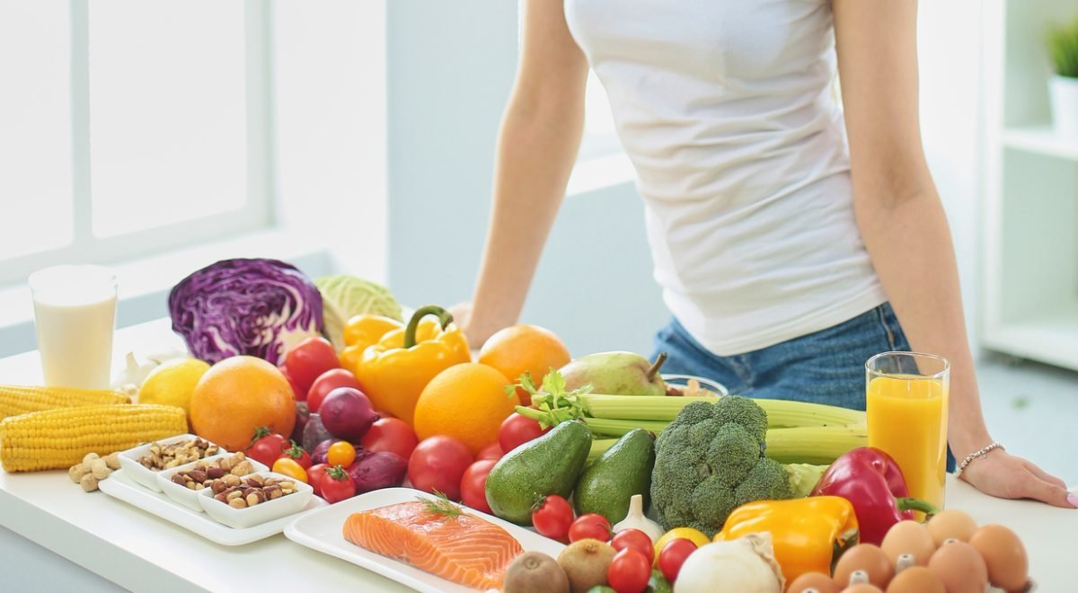 IStock - Imagem de mulher parada em frente a mesa repleta de alimentos saudáveis
