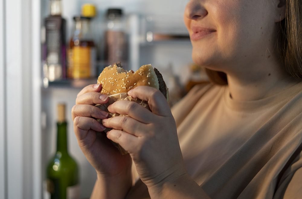 Freepik - Imagem ilustrativa de mulher comendo hambúrguer