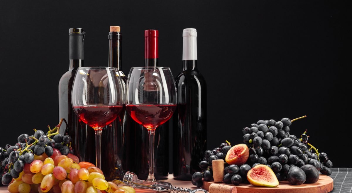 FabrikaCr/IStock - Imagem de vinhos e frutas sob uma mesa